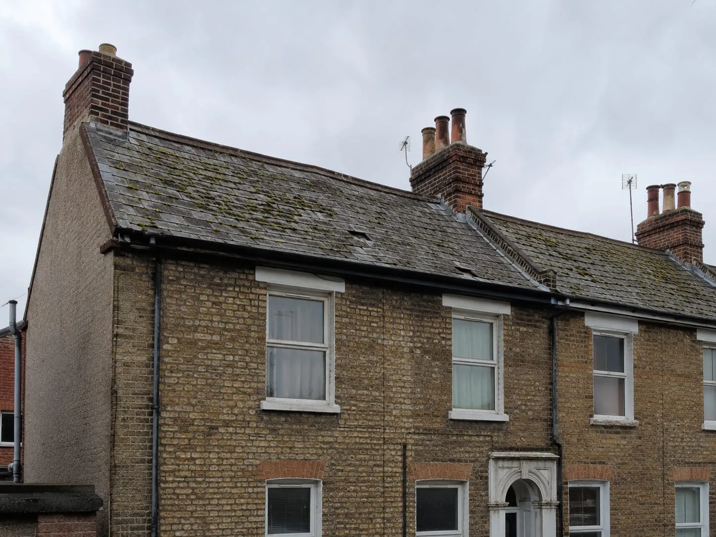 A brick terrace before work: tired slate roof, moss-covered and weathered, with slipped slates