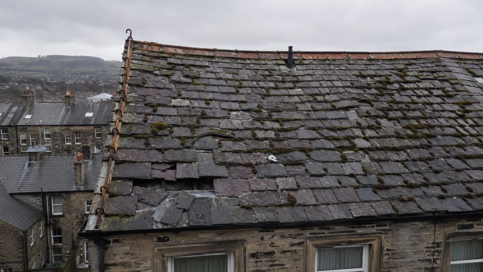 The rear roof of a Victorian stone terrace before work: weathered slate with several slipped and missing tiles, heavy moss and a sagging ridge line.